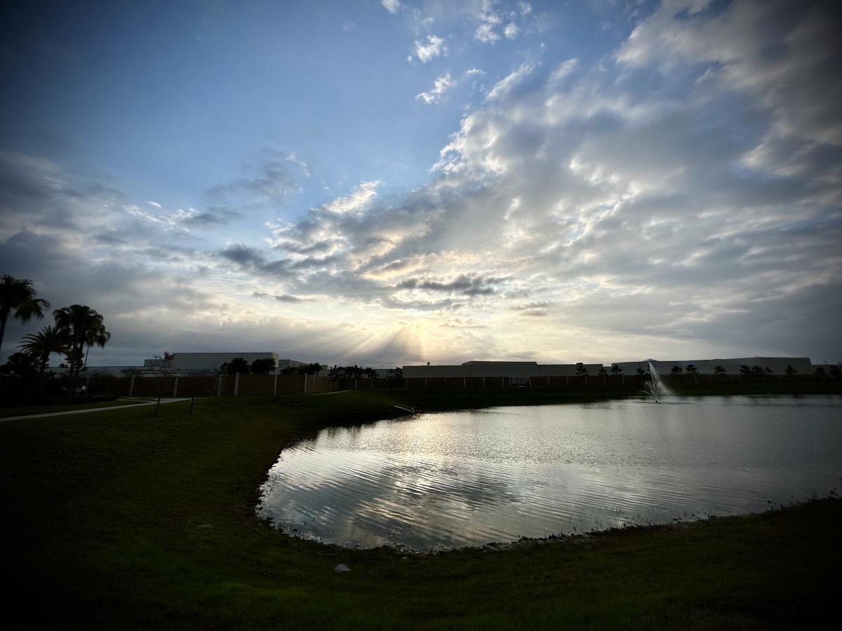 Sunrise peering through the clouds over a building and pond