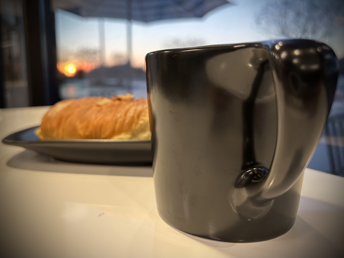 Coffee mug, croissant, and the sun rising in the background.